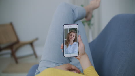 Curly-young-woman-having-video-chat-with-friends-using-mobile-phone-camera-while-lying-on-bed.-Attractive-Cheerful-Woman-Sitting-On-The-Couch-And-Having-A-Video-Call-With-GirlFriends